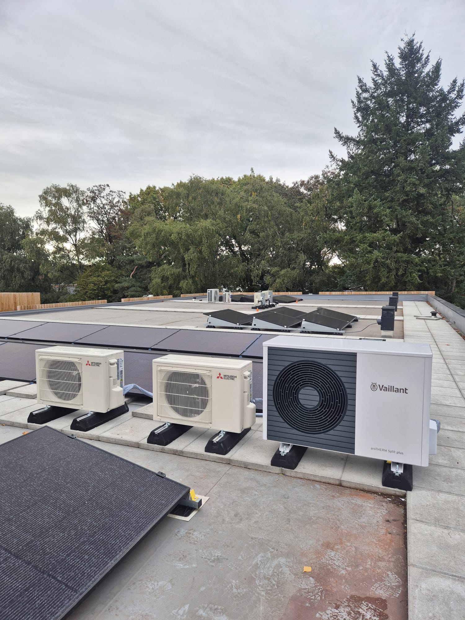 Vaillant aroTHERM Split plus warmtepomp en 2 Mitsubishi Electric airco-buitenunits op plat dak van bedrijfspand, naast zonnepanelen
